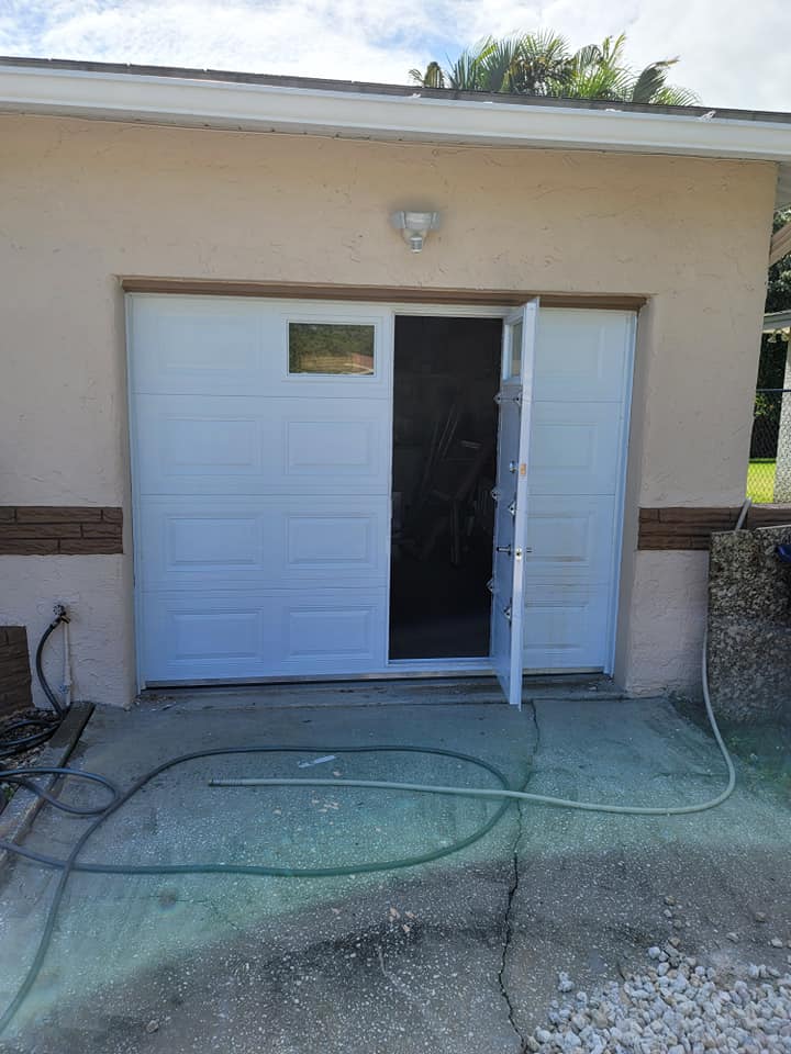 A white garage door with the door open and a hose in front of it.