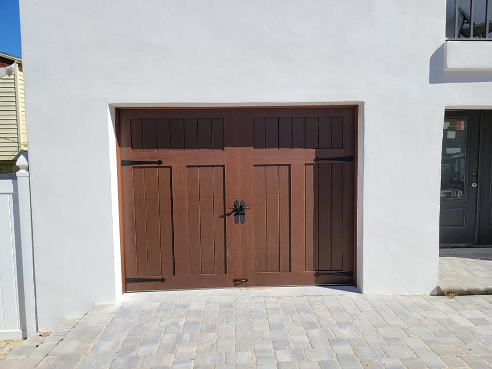 A white house with a wooden garage door and a brick driveway.