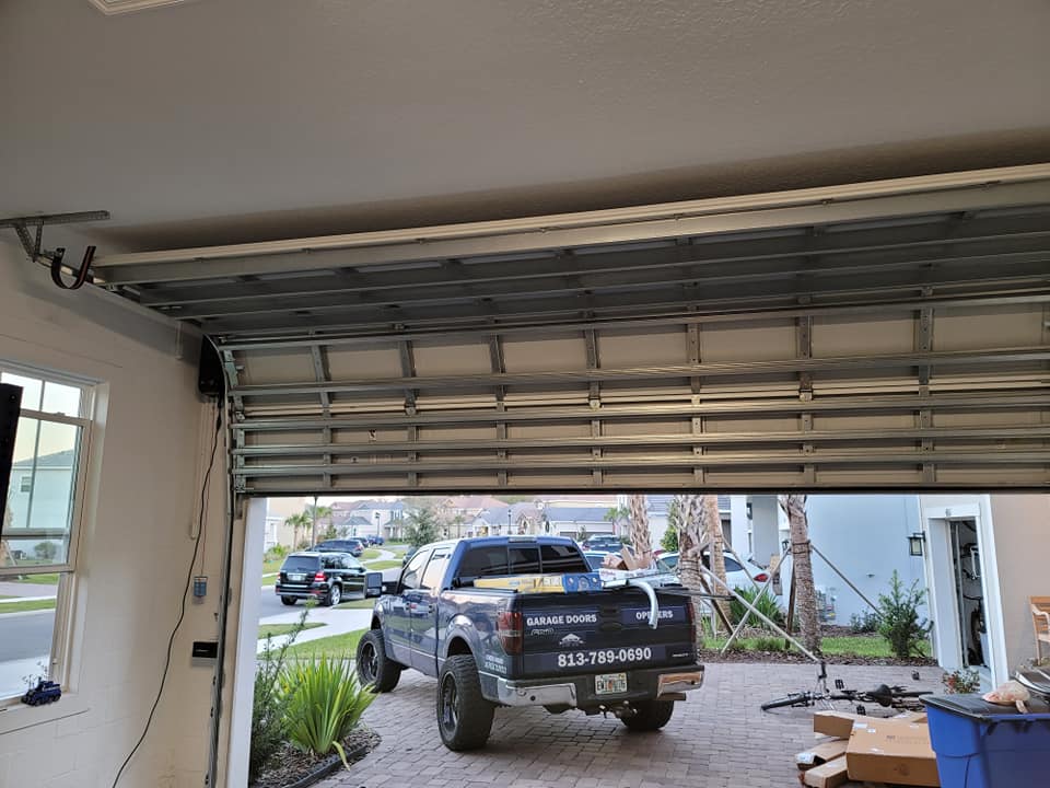 Garage door open being repaired with a pickup truck inside, looking out to a residential street.