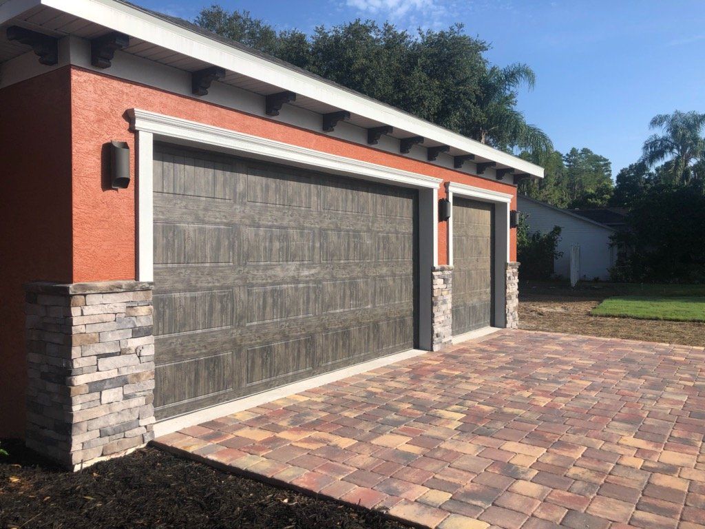A garage with two garage doors and a brick driveway.