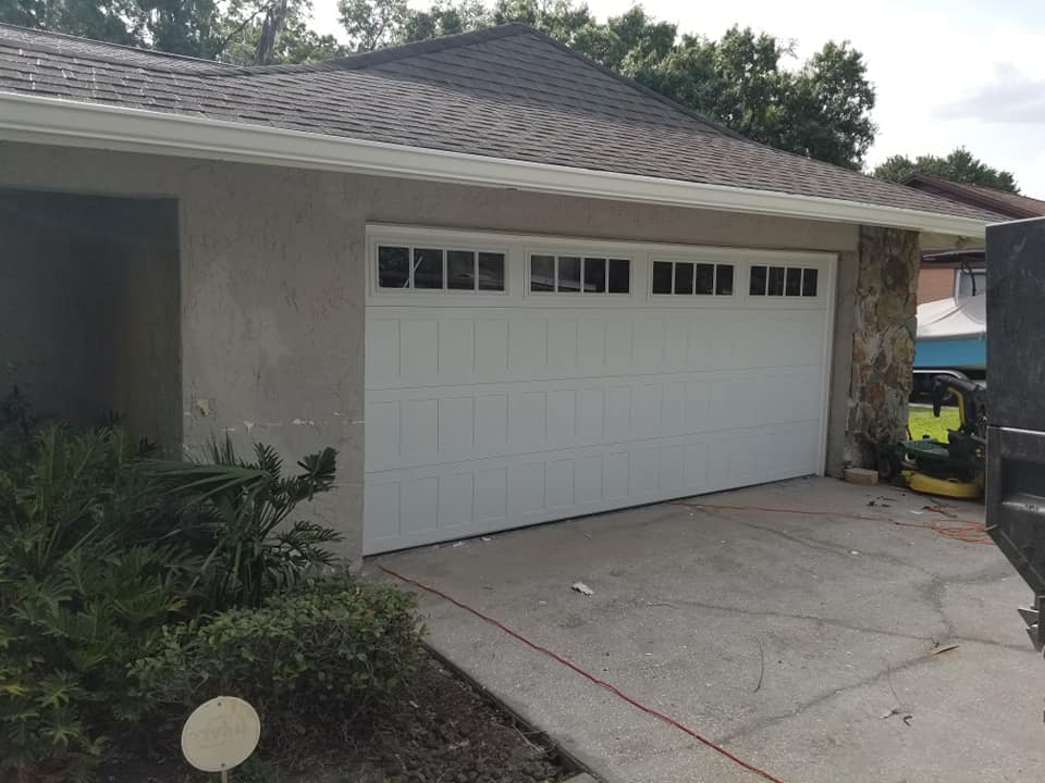 A white garage door with windows is sitting in front of a house.