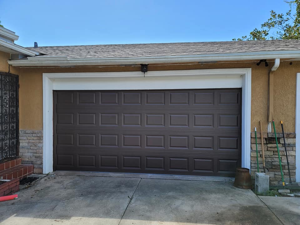 A brown garage door is sitting in front of a house.