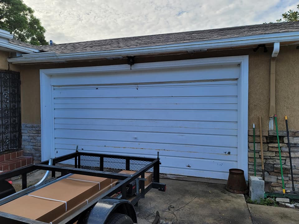 A white garage door with a trailer parked in front of it.
