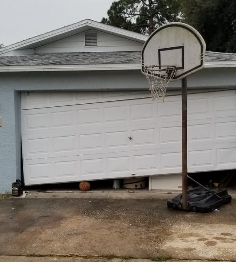 A basketball hoop is in front of a garage door that is broken