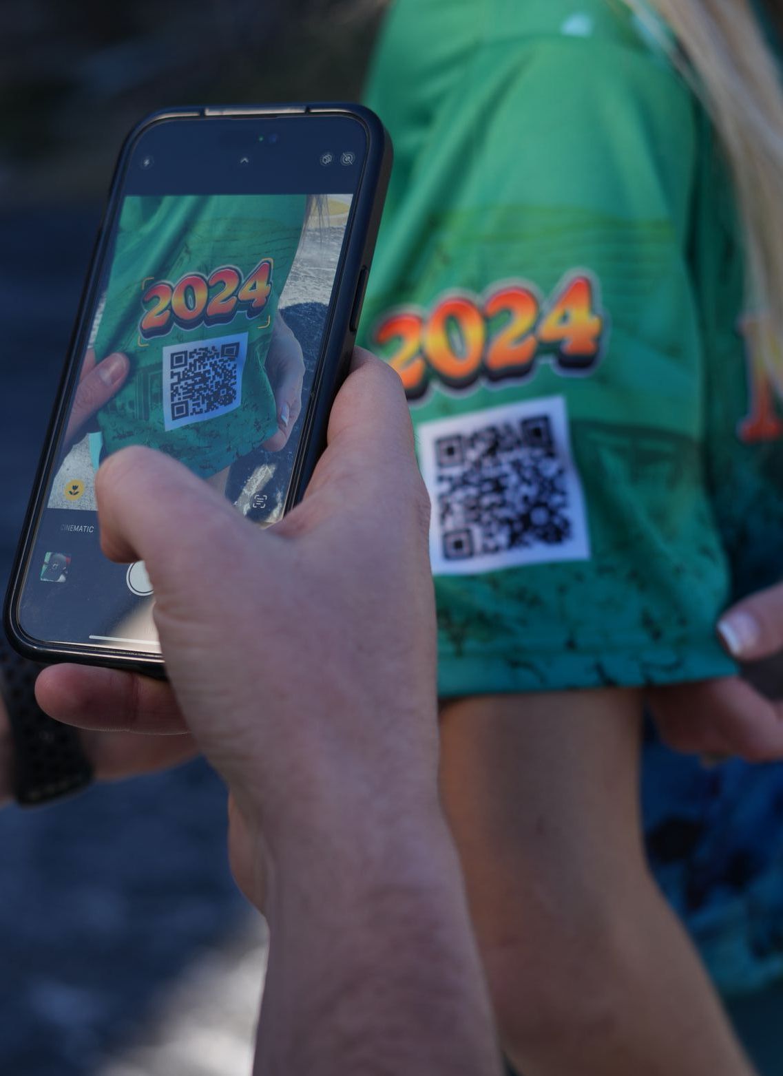 A person is taking a picture of a person wearing a green shirt that says 2024