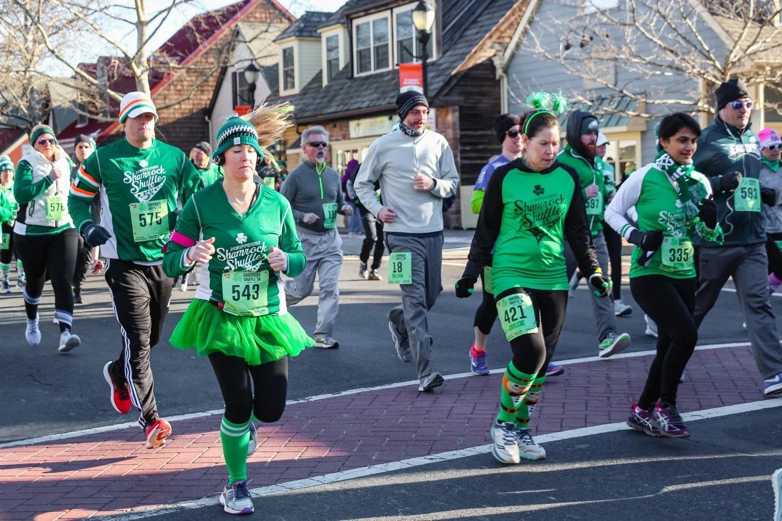 A group of people are running down a street wearing green shirts and skirts.