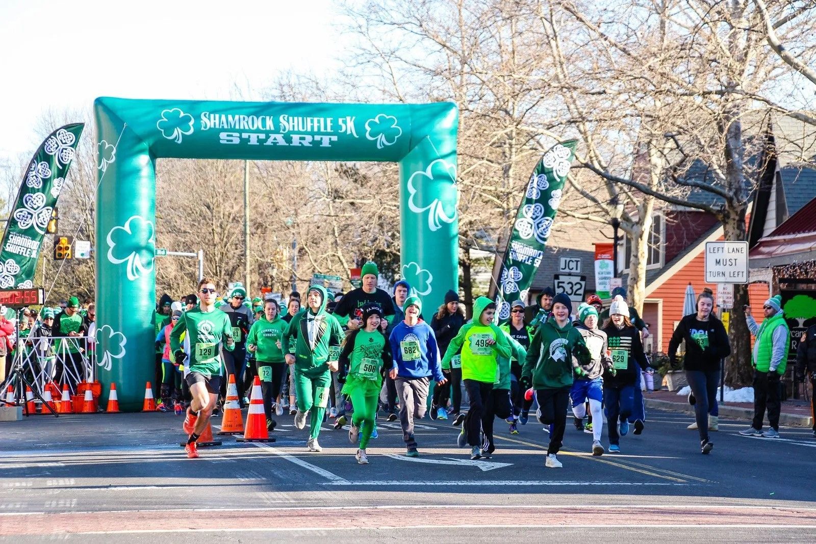 A group of people in green shirts are running down a street.