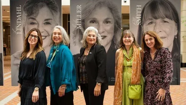A group of women are posing for a picture in front of a large poster of a woman.
