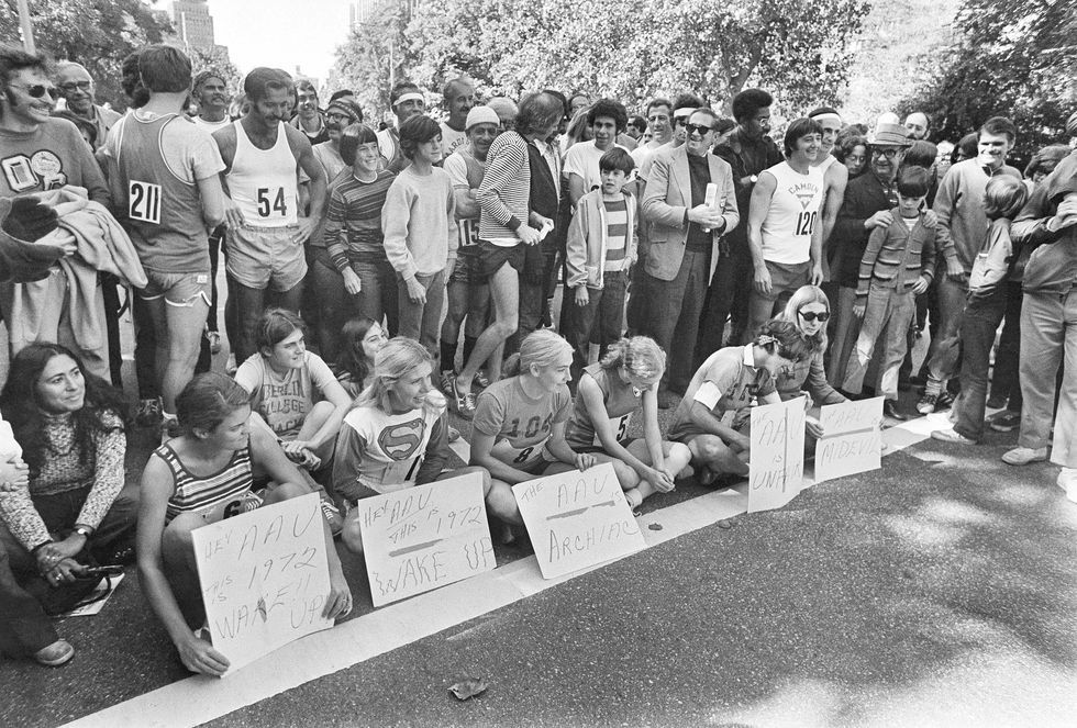 A group of people are sitting on the side of the road holding signs.