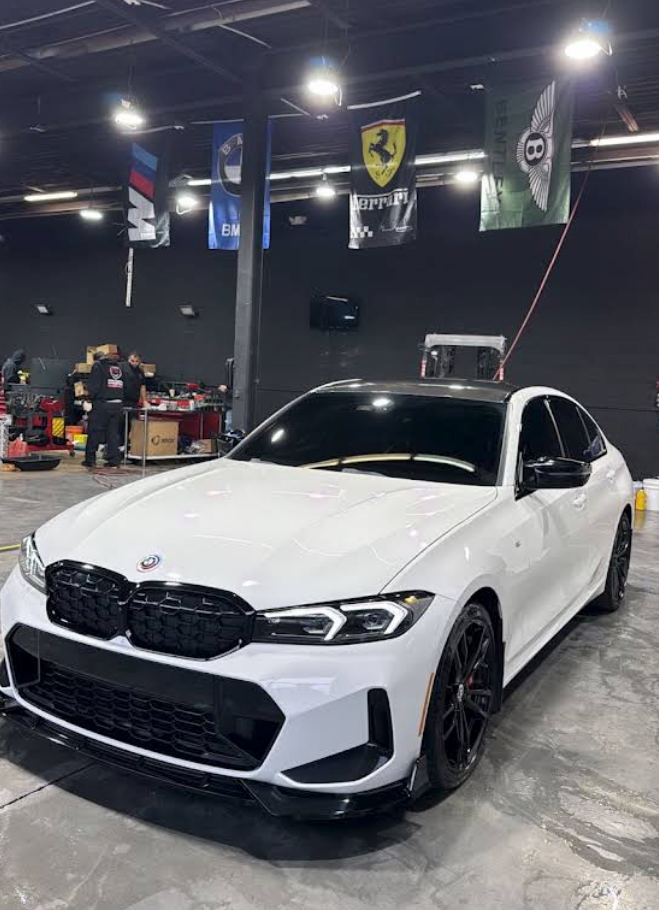 White BMW sedan in a garage, angled front view, with black wheels and a large black grille. | SA Performance