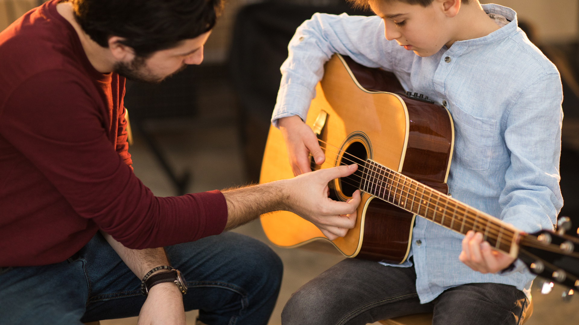 Adult and child playing acoustic guitar together on a couch