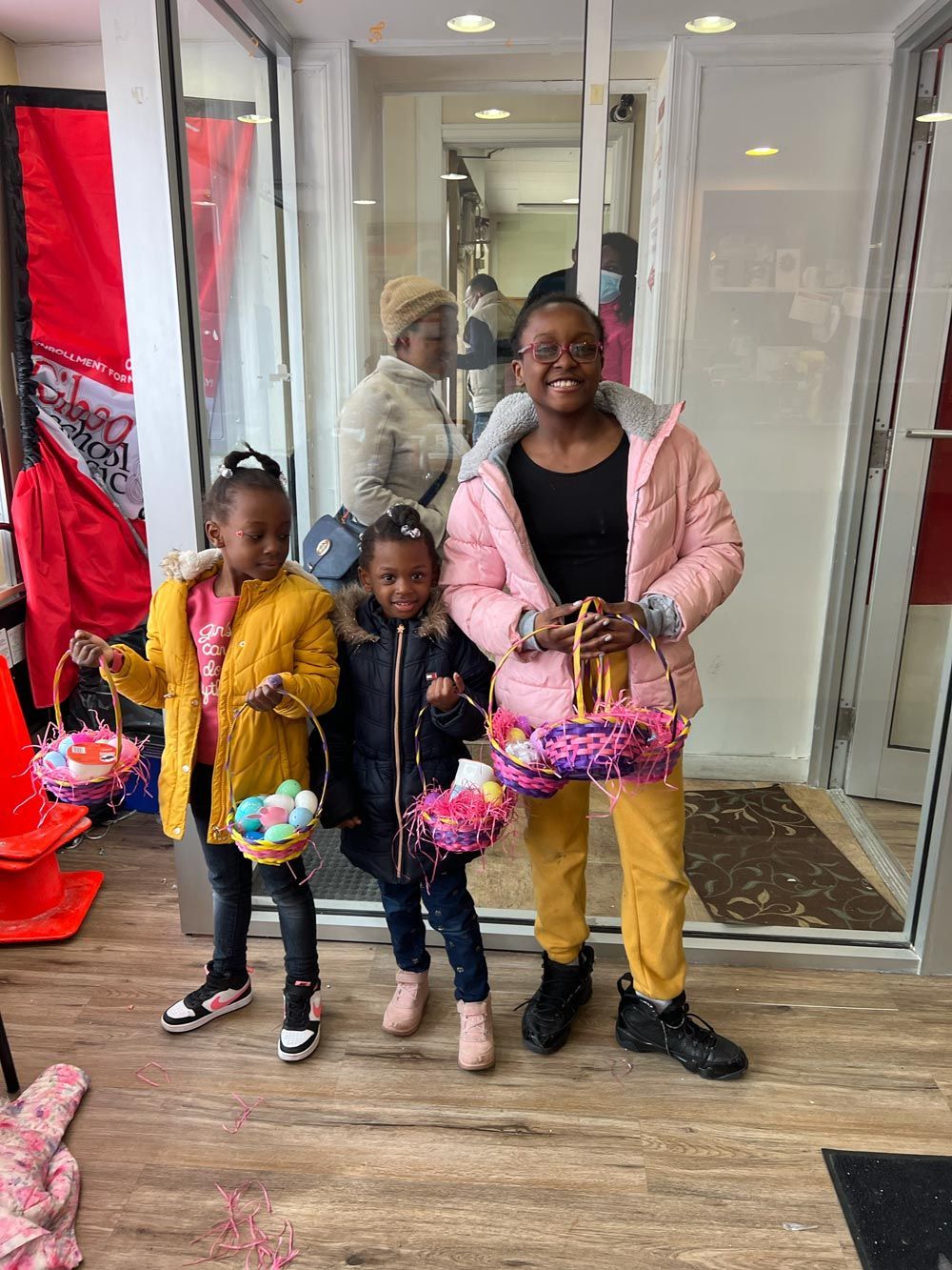Three children holding colorful gift bags at a doorway, smiling in a decorated indoor entryway.