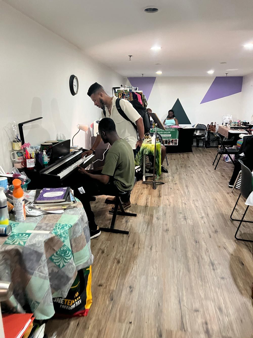 Man and boy near a black piano in a bright room with wood floors and tables along the wall