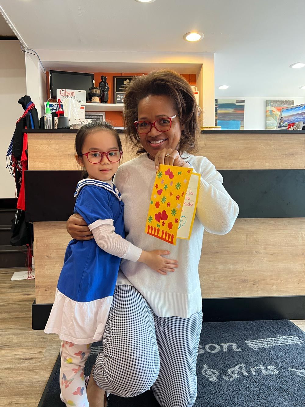 Two people hugging in a lobby, holding a yellow patterned bag and a striped tote.