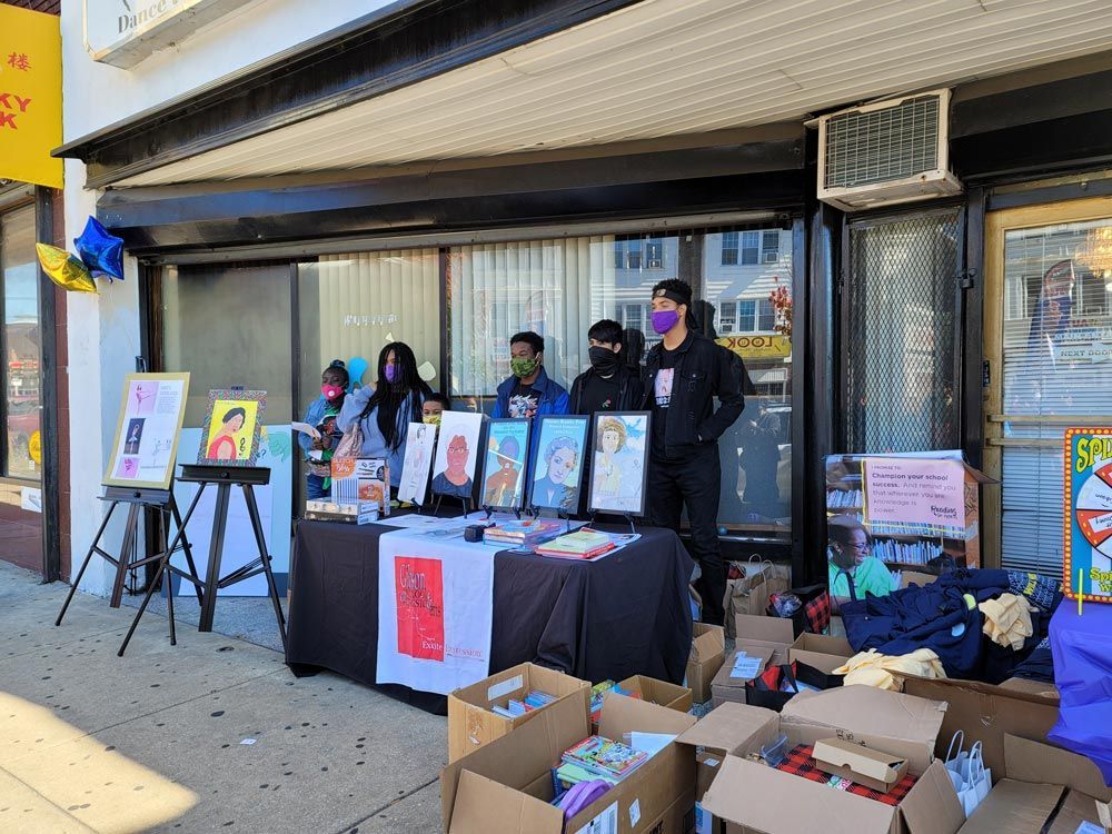 People behind a table of framed prints and donations outside a storefront
