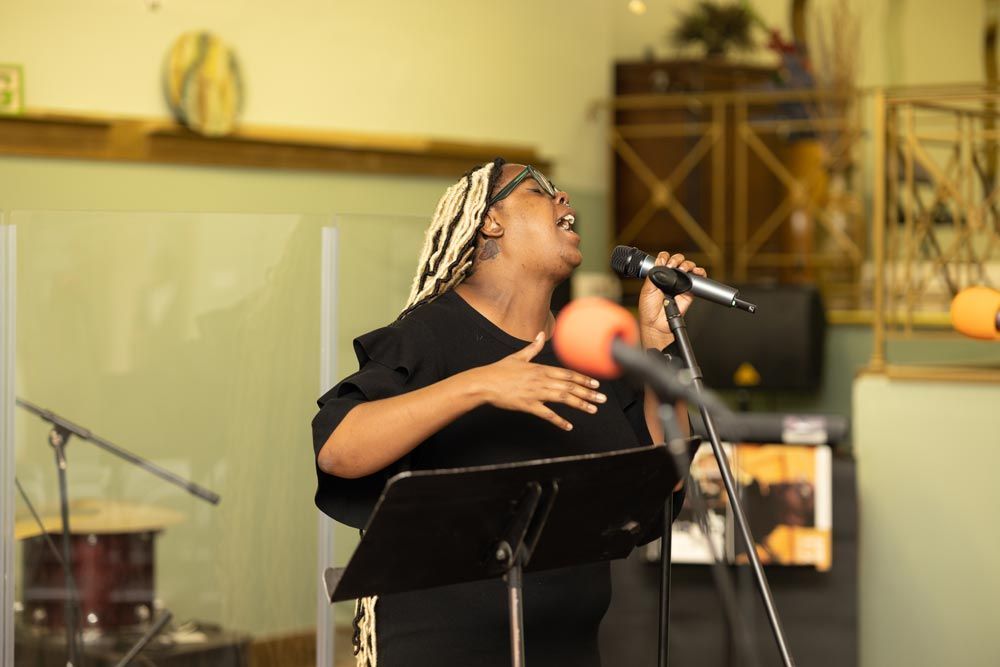 Singer performing into a microphone on a stage, wearing a black outfit and patterned headscarf.