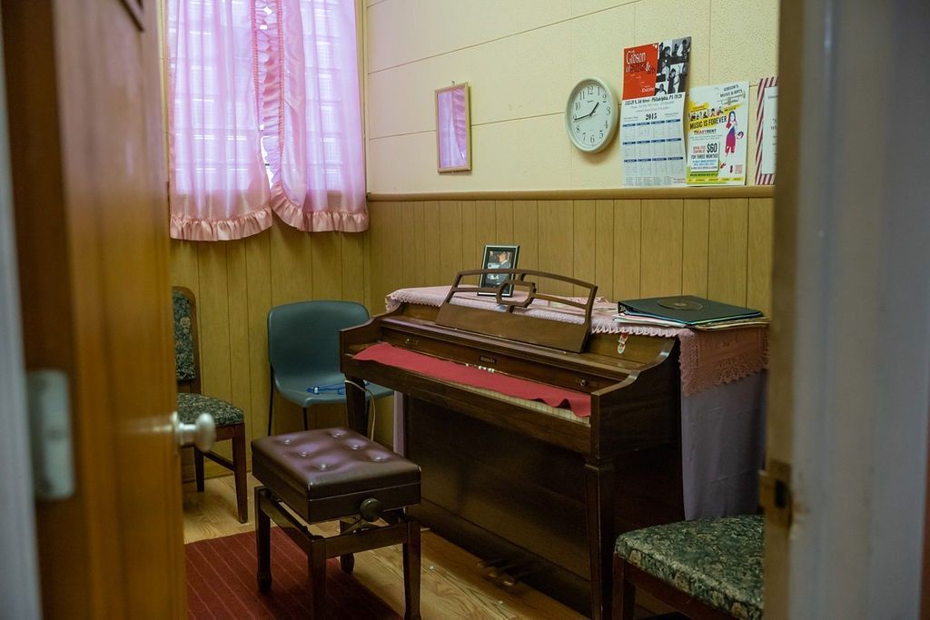 Small music room with an upright piano, bench, clock, and pink curtains