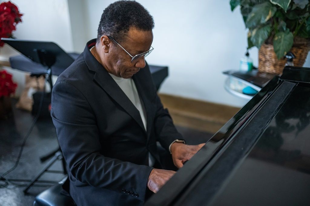 Man playing a black grand piano indoors, focused on the keys.