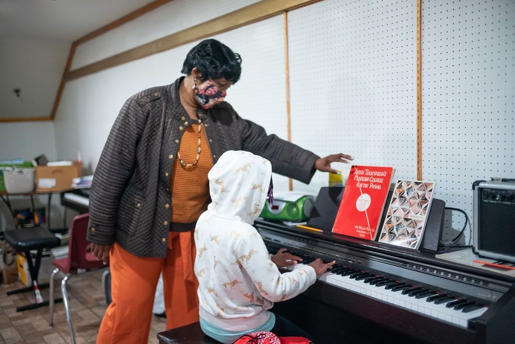 Teacher guiding a child at a keyboard in a bright music room