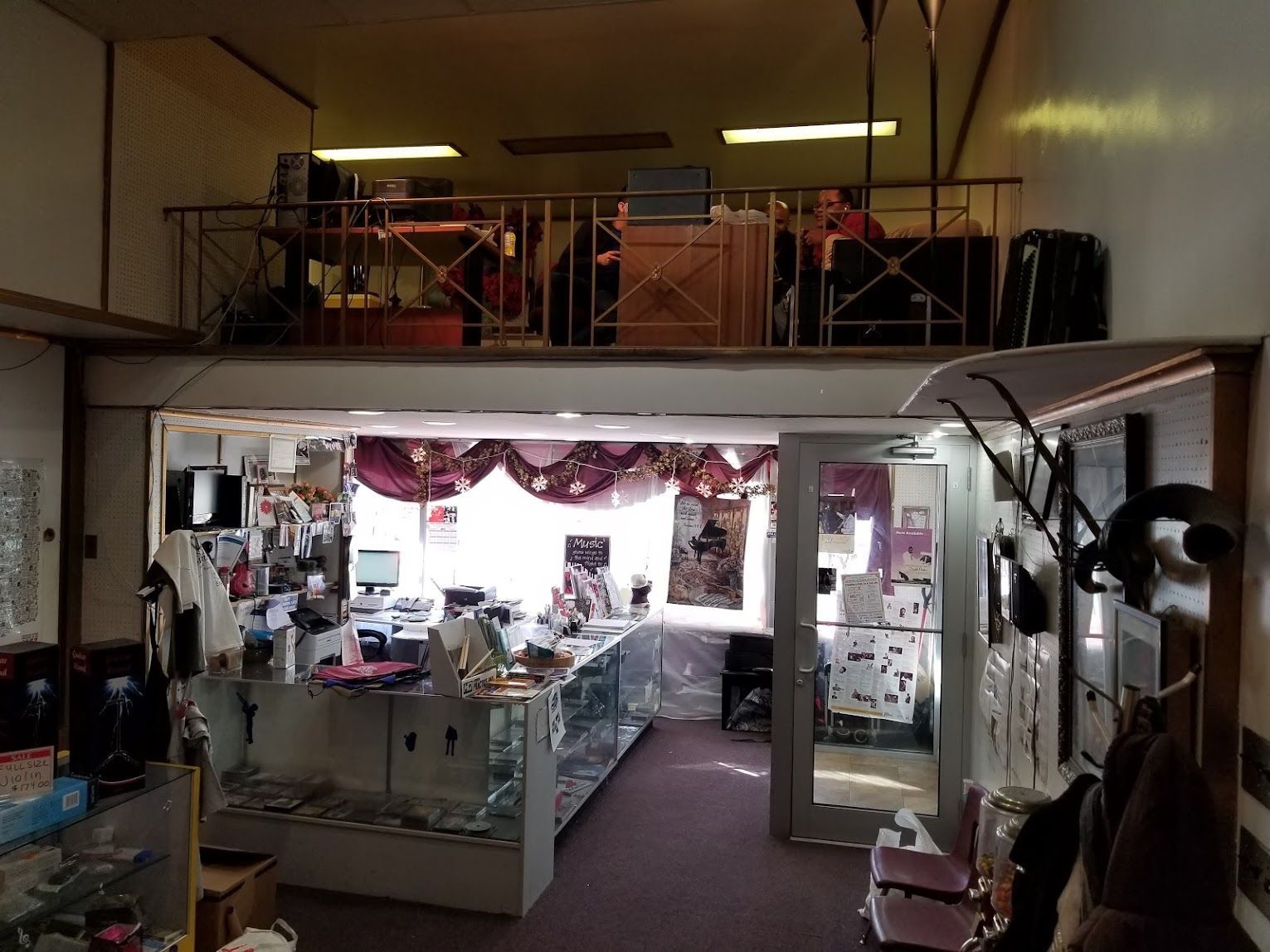 Dim interior of a cluttered store or workshop with glass display cases, shelves, and loft area above