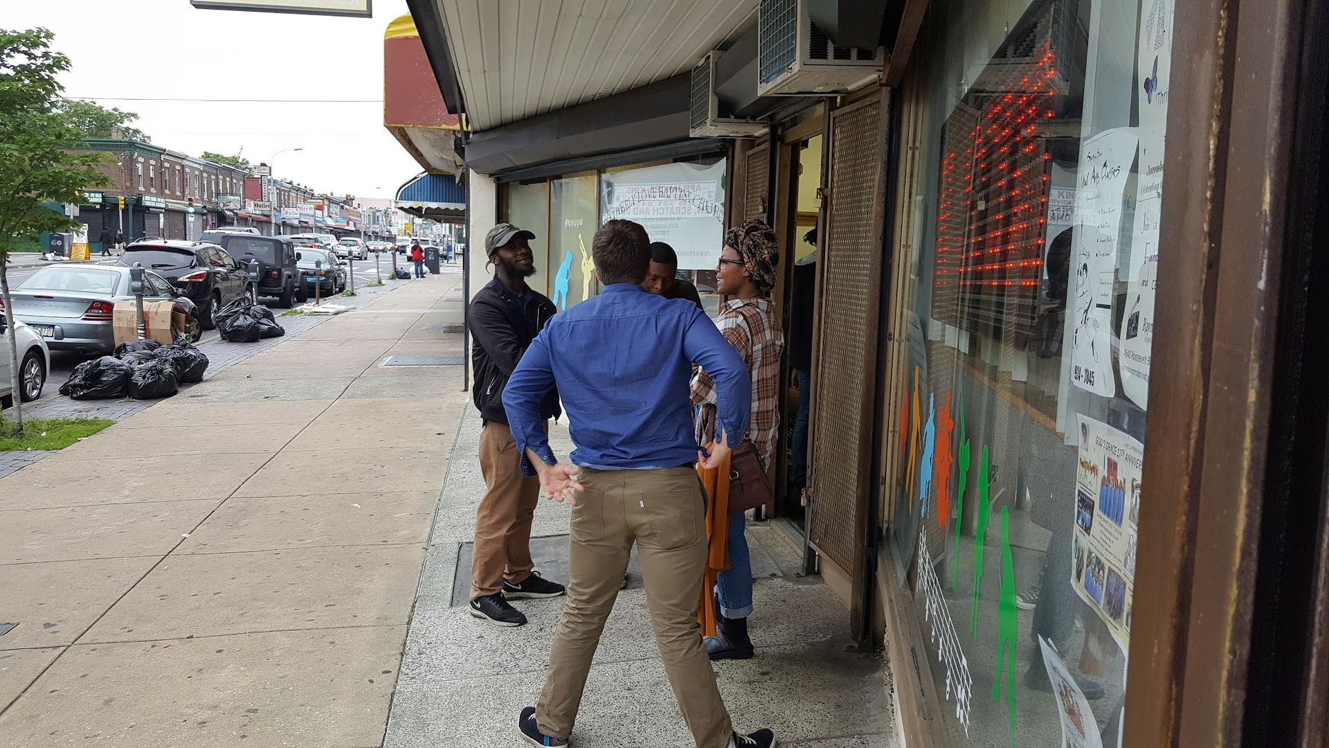 People standing on a city sidewalk outside a storefront, one in a blue shirt near the entrance