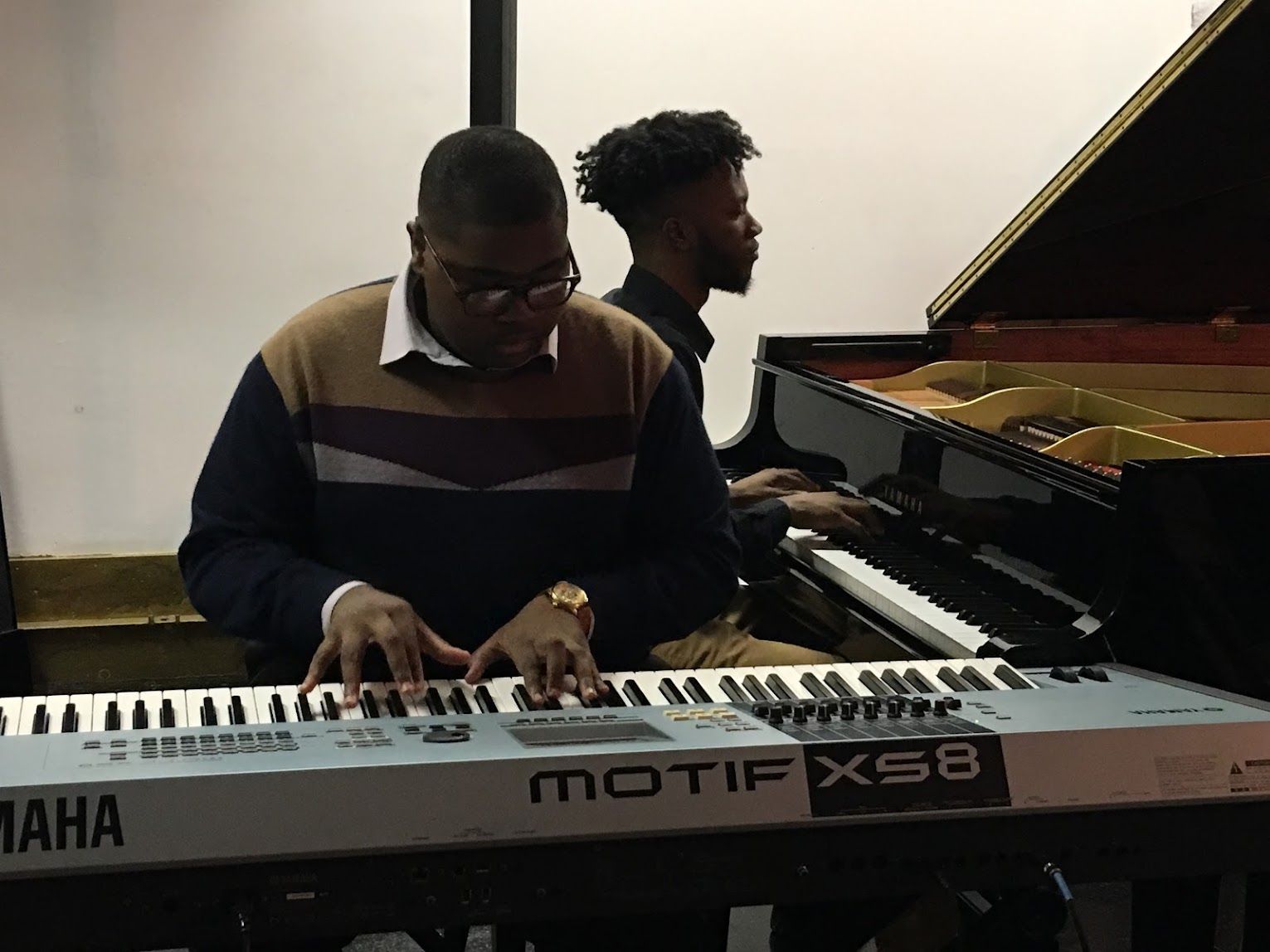 Two musicians play keyboard and piano side by side in a room.