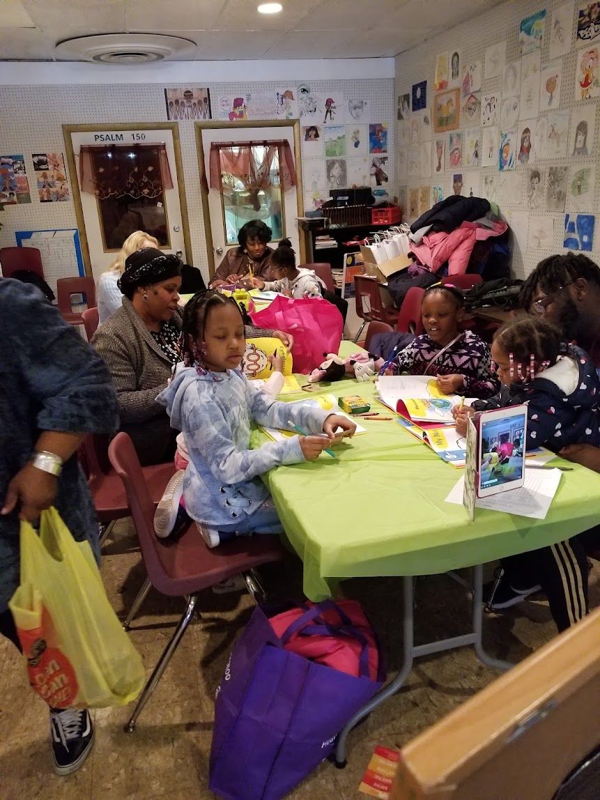 Children crafting at a long table in a colorful classroom with drawings on the walls
