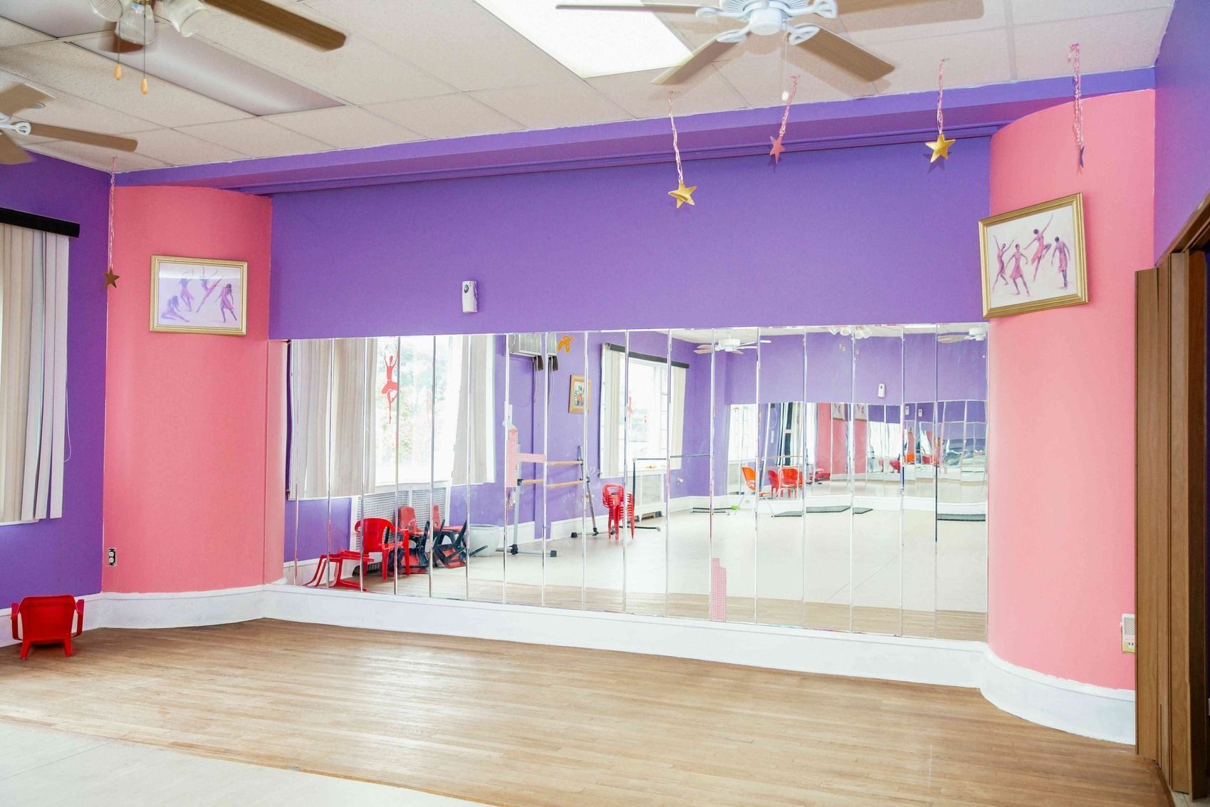 Empty dance studio with mirrored wall, purple and pink walls, and wooden floor