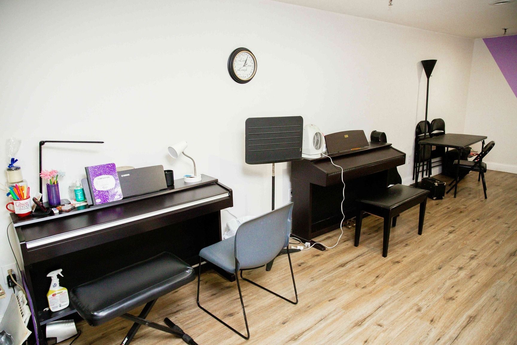 Music room with two pianos, benches, and a wall clock on a wooden floor
