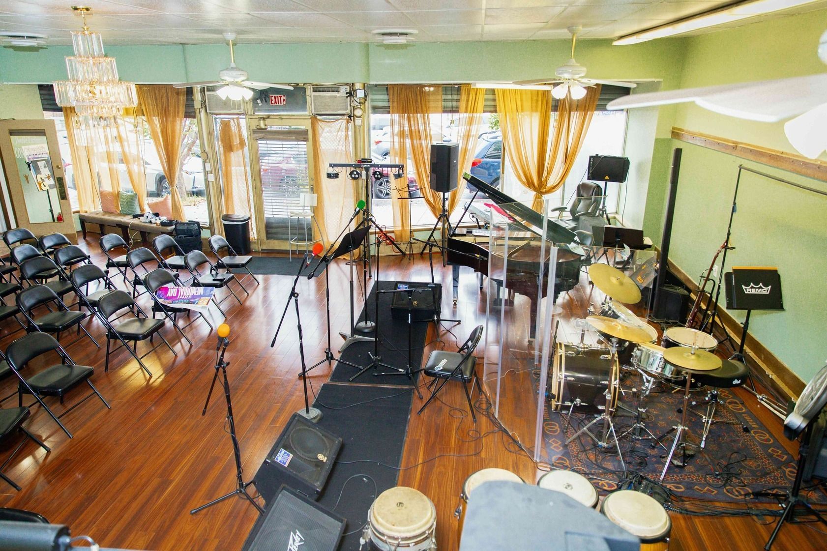 Empty music rehearsal room with drum kit, guitars, microphones, and chairs on a wooden floor