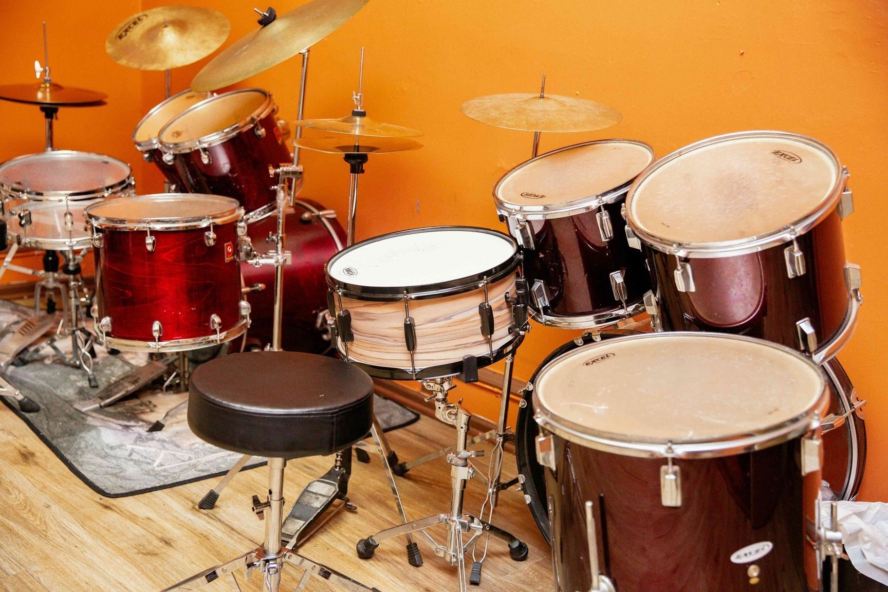 Red drum kit with cymbals on a rug against an orange wall in a studio or rehearsal space