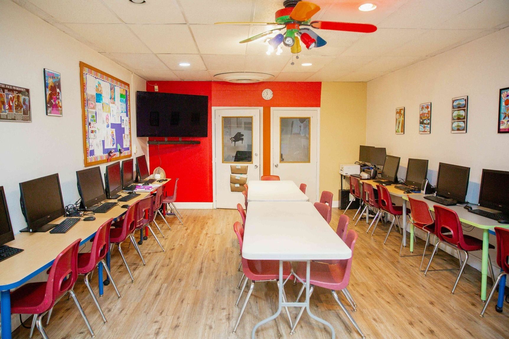 Computer lab with rows of desks, desktop monitors, red chairs, and bright red walls