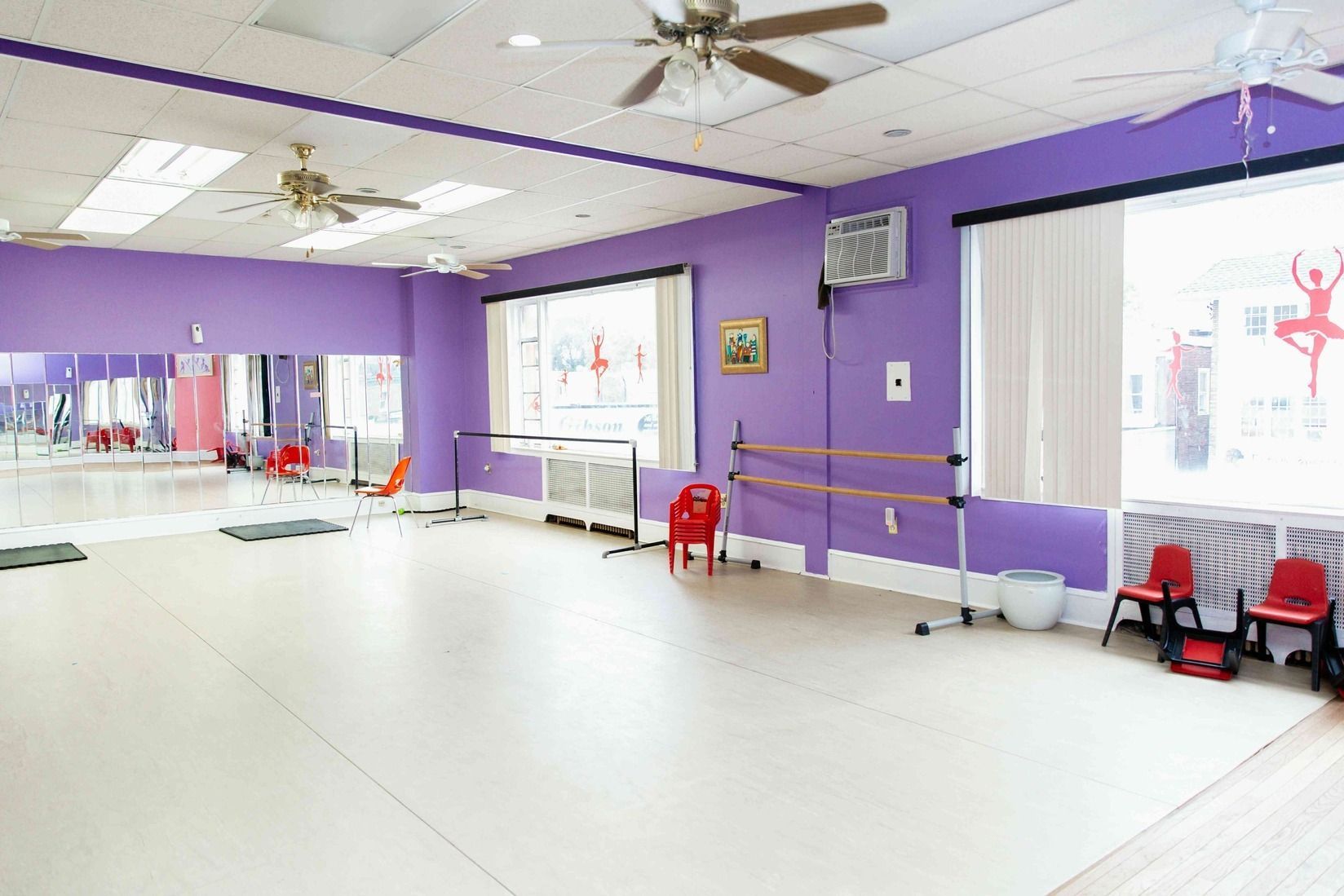 Empty dance studio with purple walls, mirrors, ballet barre, and white floor