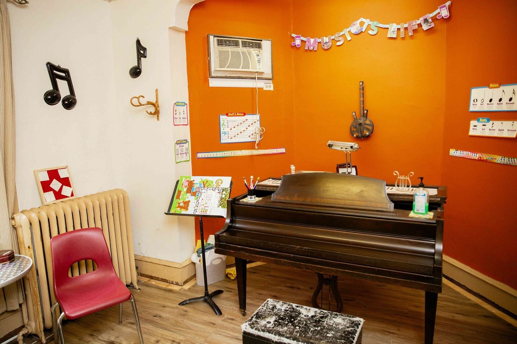 Small music room with a grand piano, orange accent wall, musical decor, and a pink chair