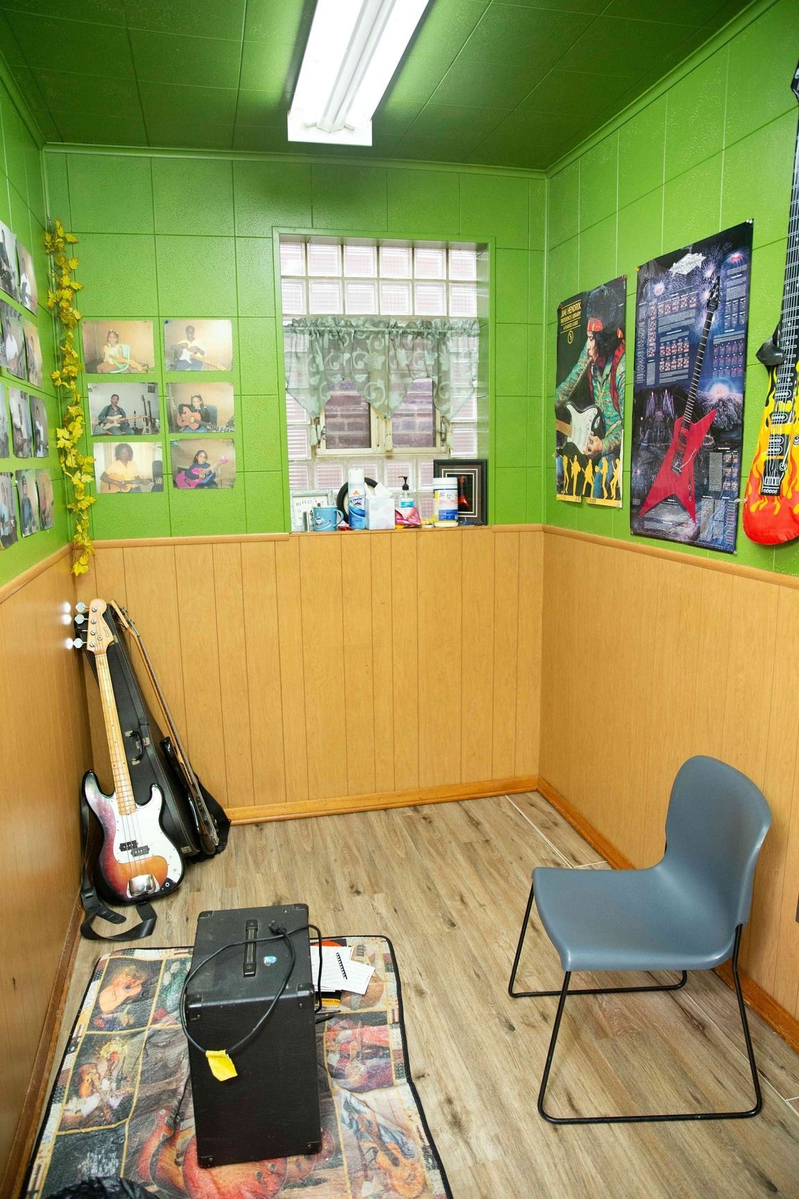 Small music room with green walls, guitars, posters, a chair, and a pedal/amp on the floor.