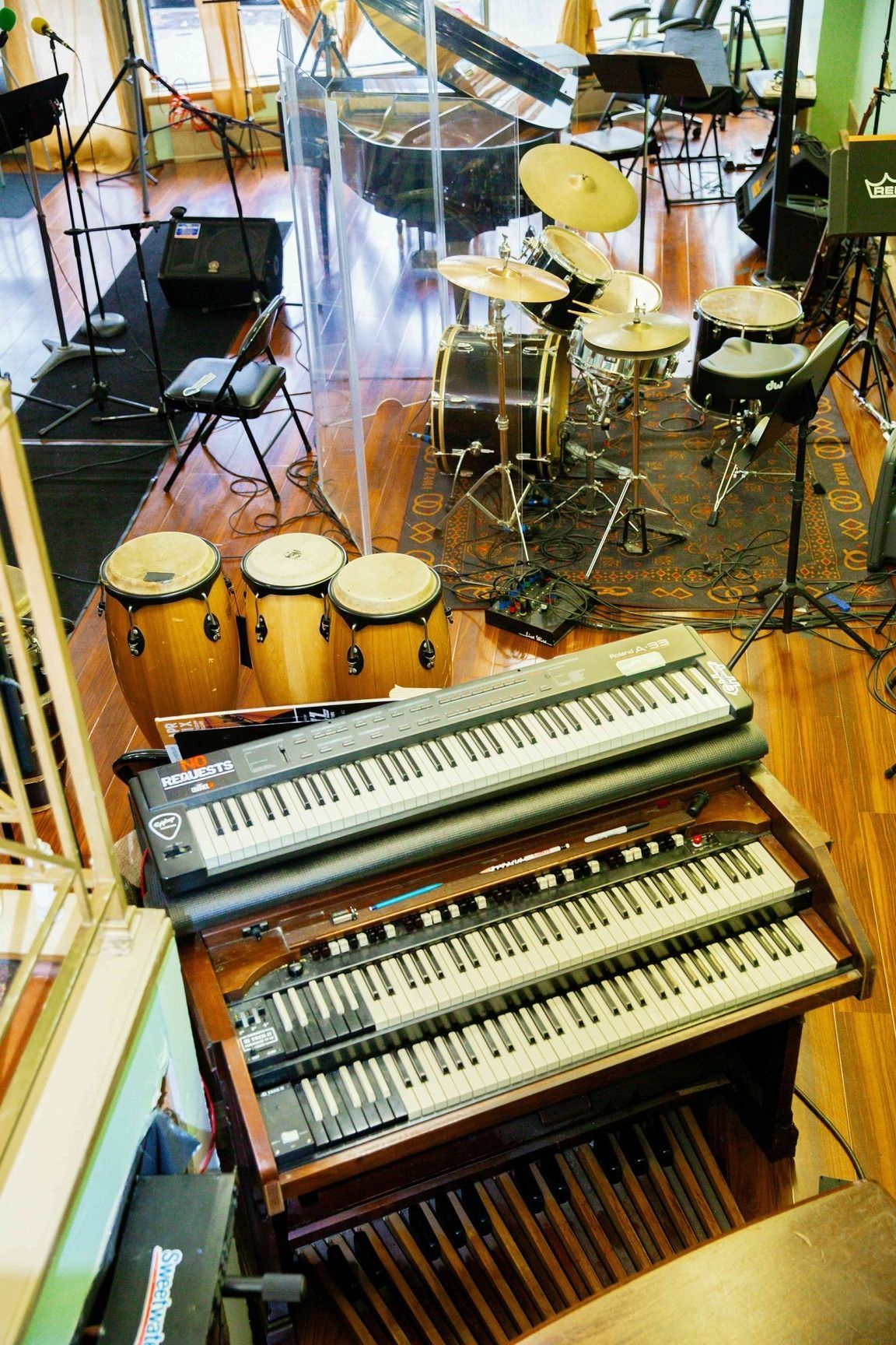 Music studio with drums, congas, and two keyboards on a wood floor
