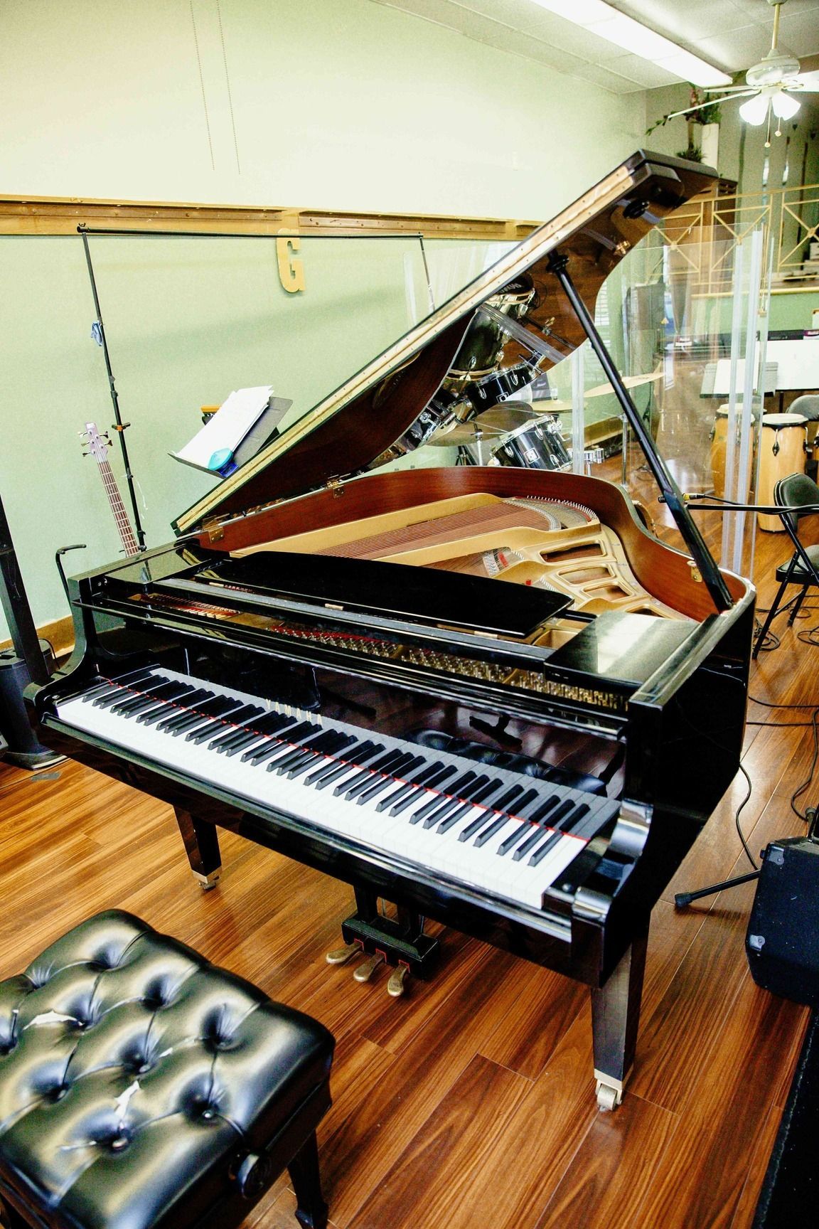 Black grand piano with lid open in a music studio, showing keys and a tufted bench.