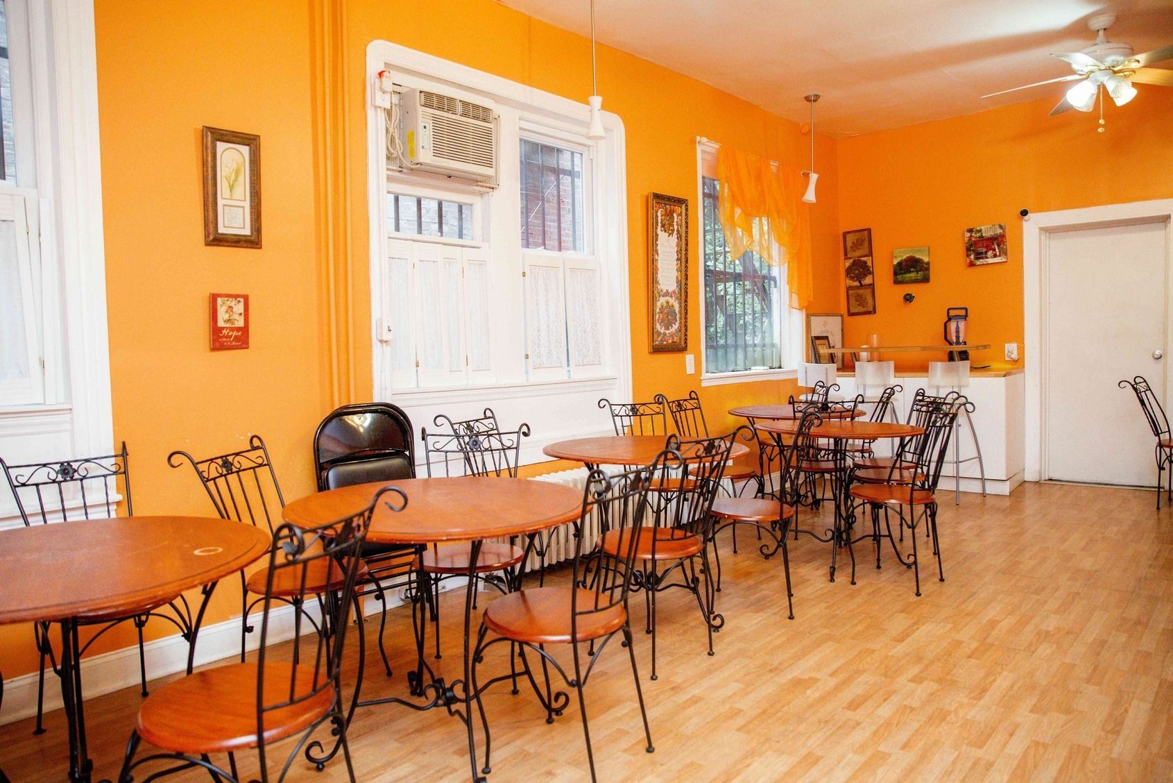 Bright orange cafe interior with empty tables, metal chairs, and a white door and windows.