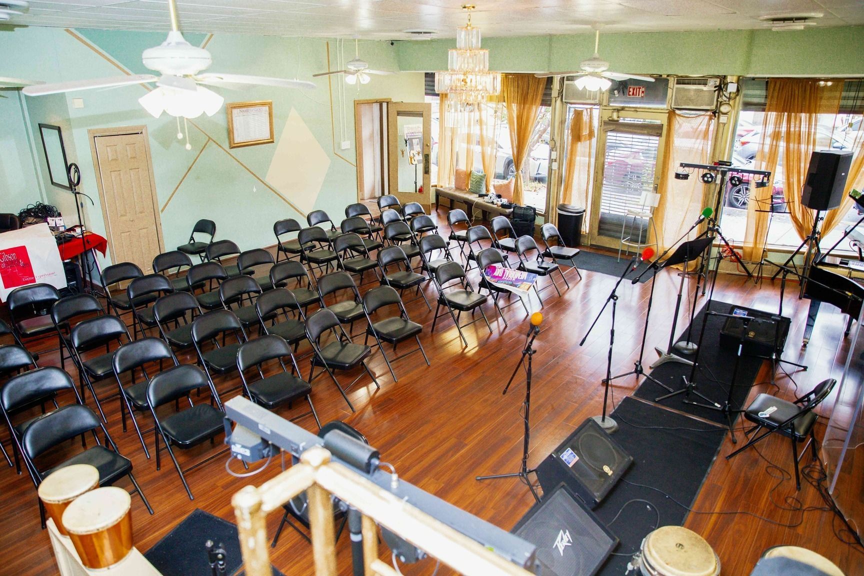 Empty music venue with rows of black chairs, stage equipment, and microphones on a wooden floor