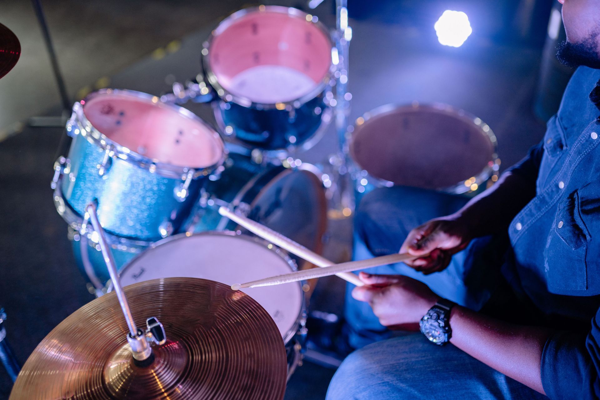 Drummer playing blue drum kit with sticks on cymbal and snare under stage lights