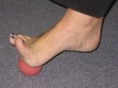 Foot on a red ball, rolling across a gray carpet.