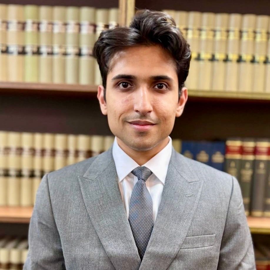 Portrait of a man in a gray suit standing in front of law books in a library