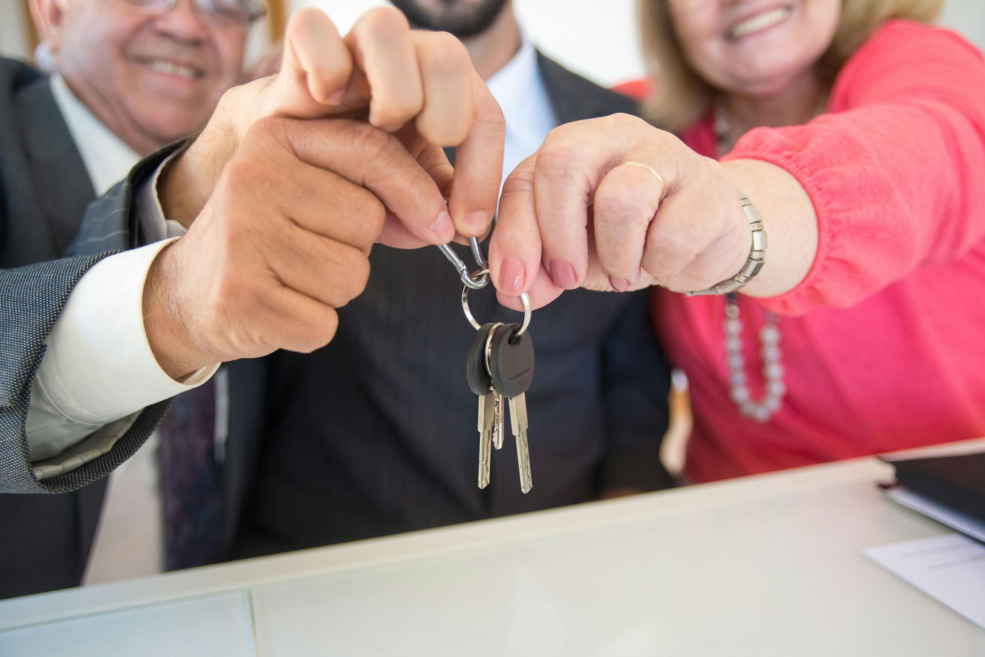 Hands joining a key ring at a business desk, with smiling people in the background