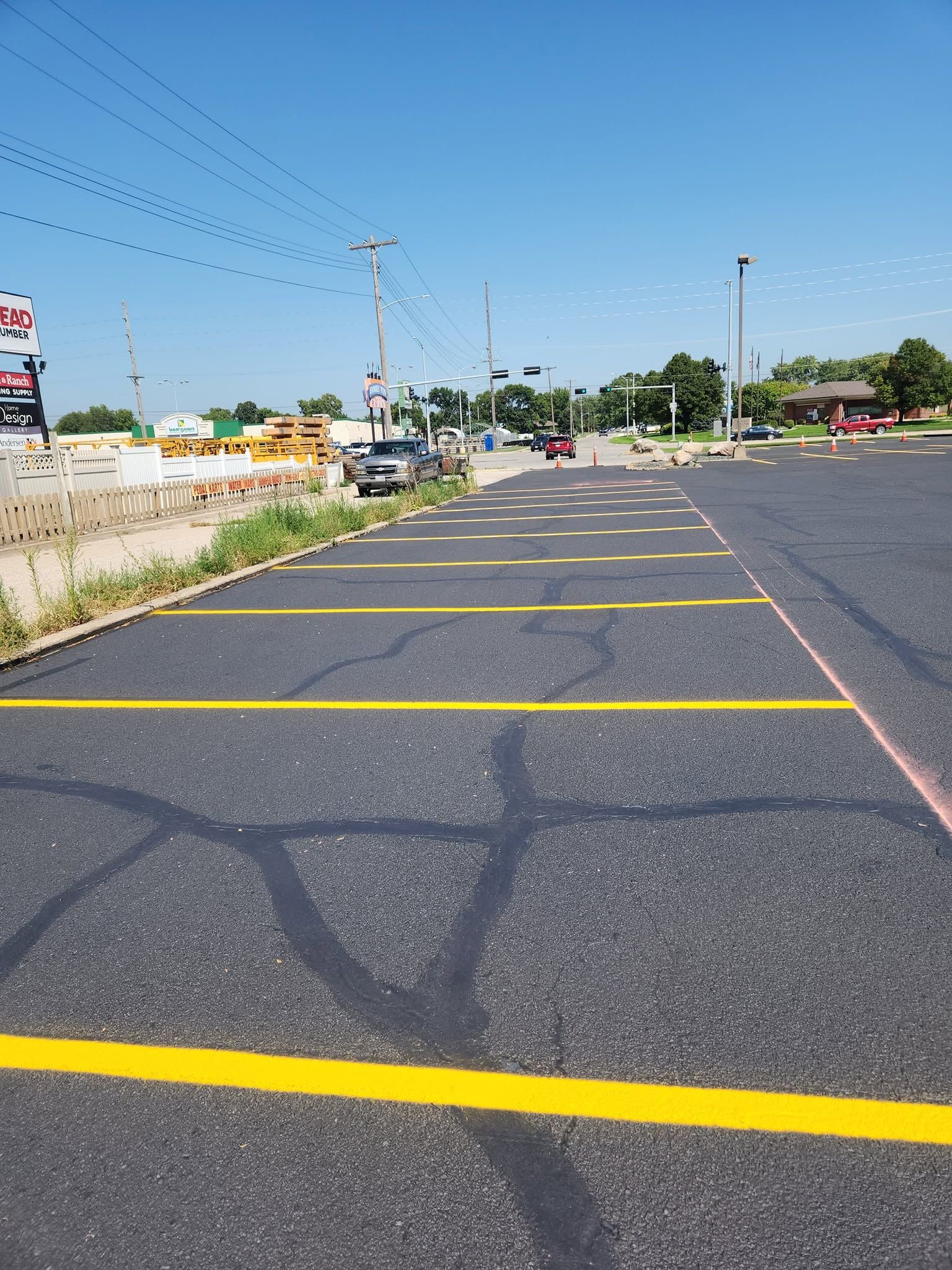 Empty asphalt parking lot with yellow lines beside a road under a clear blue sky