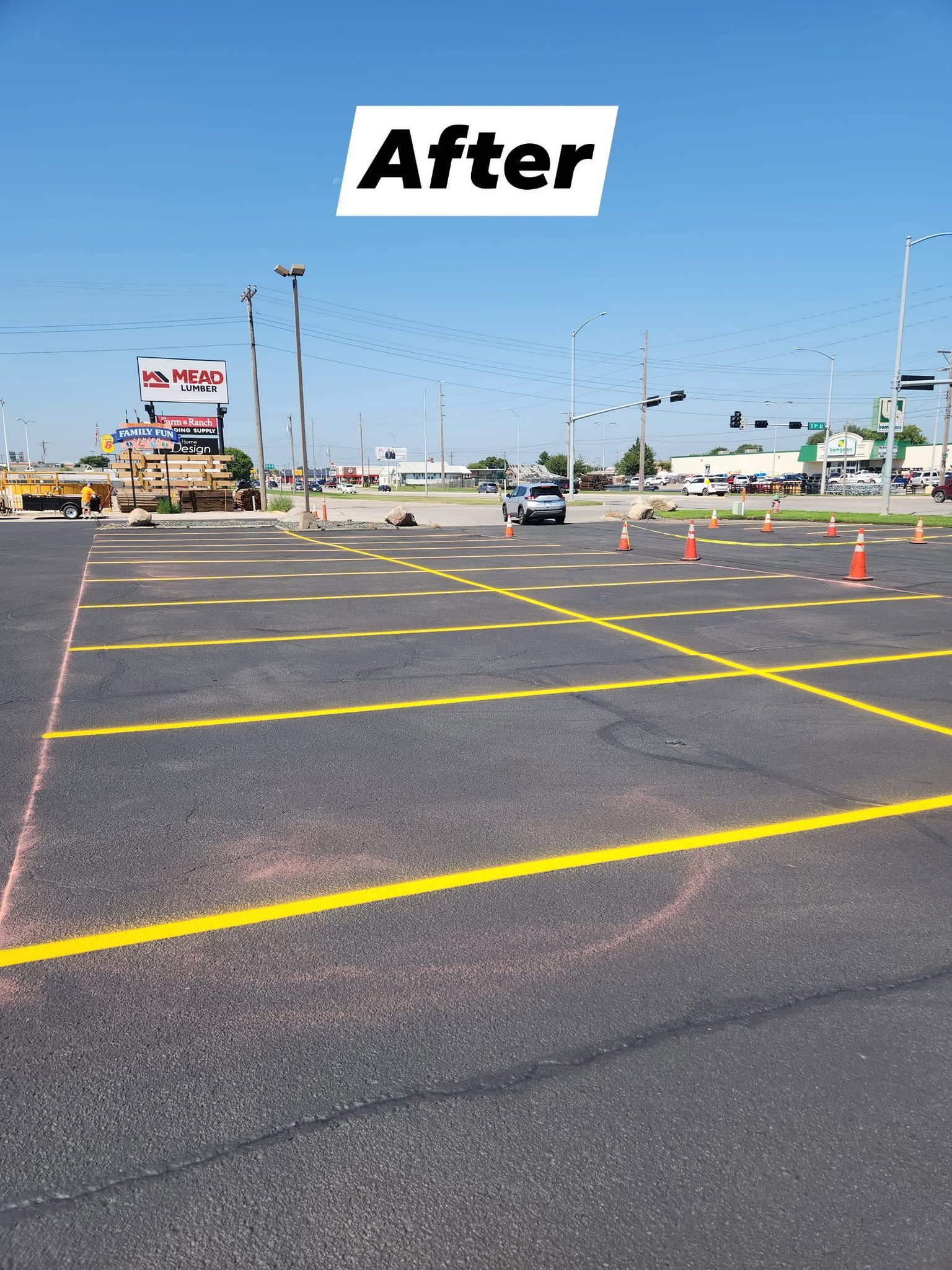 Freshly painted yellow parking lot lines and cones in an empty asphalt lot under a clear blue sky