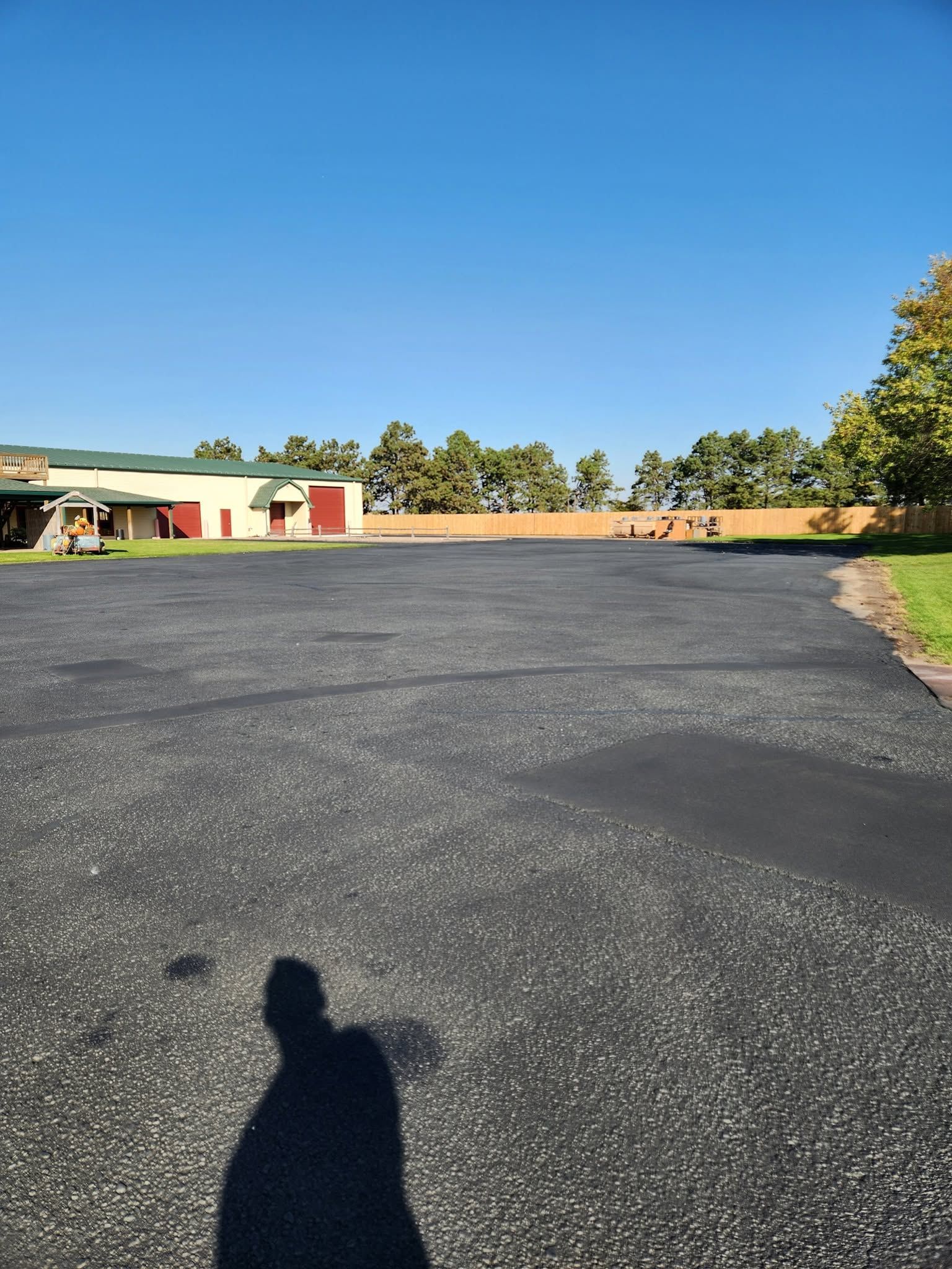 Wide paved lot beside a low building and trees under a clear blue sky