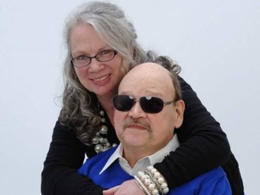 Smiling woman hugging a man in sunglasses against a light background