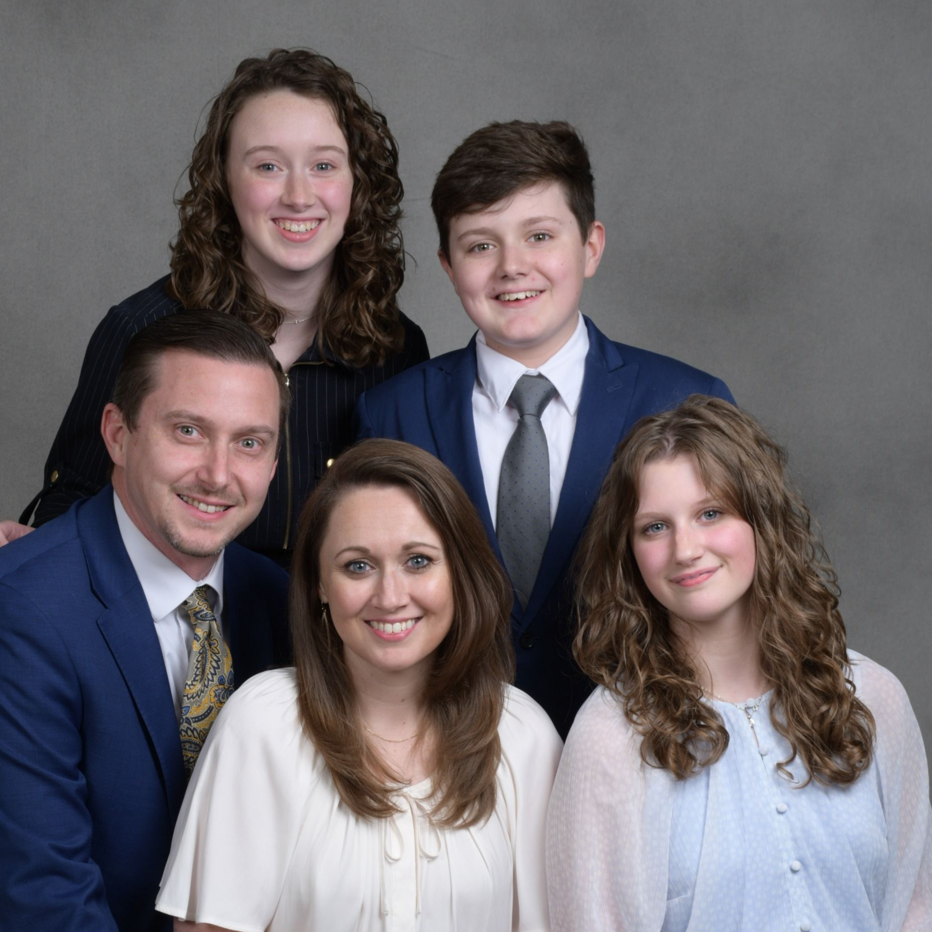 Family of five posing in a studio, wearing coordinated blue and white outfits, smiling at the camera
