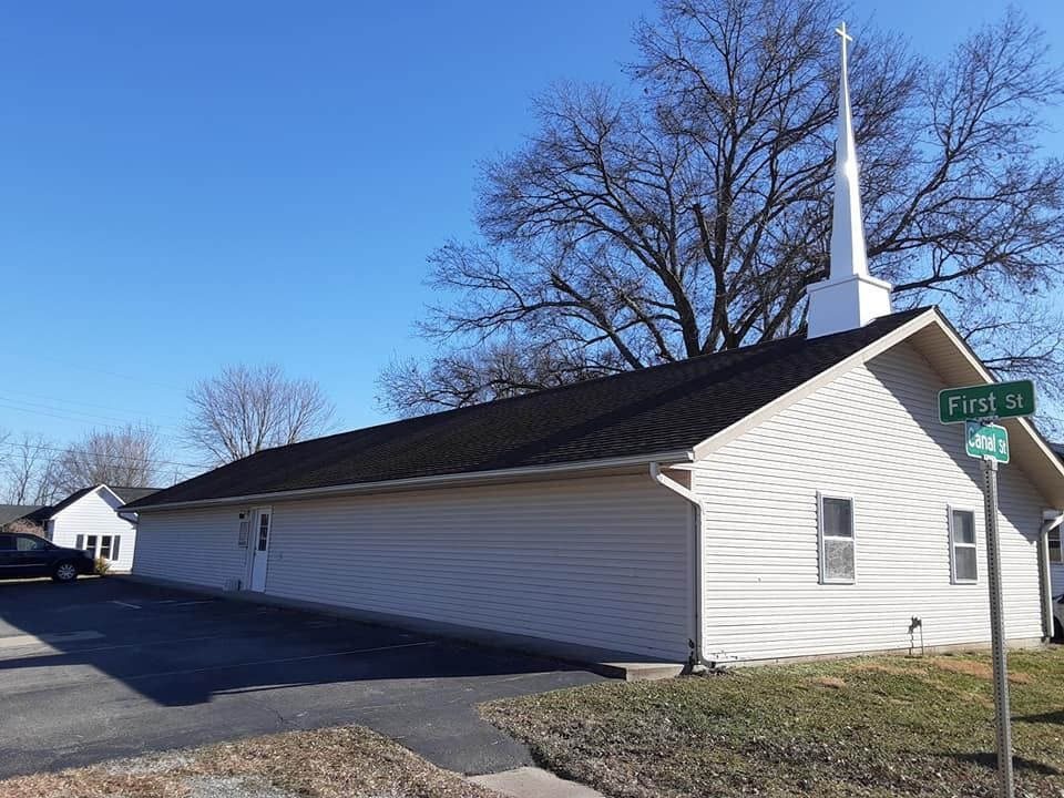 White church with a tall steeple on a sunny street corner under a blue sky