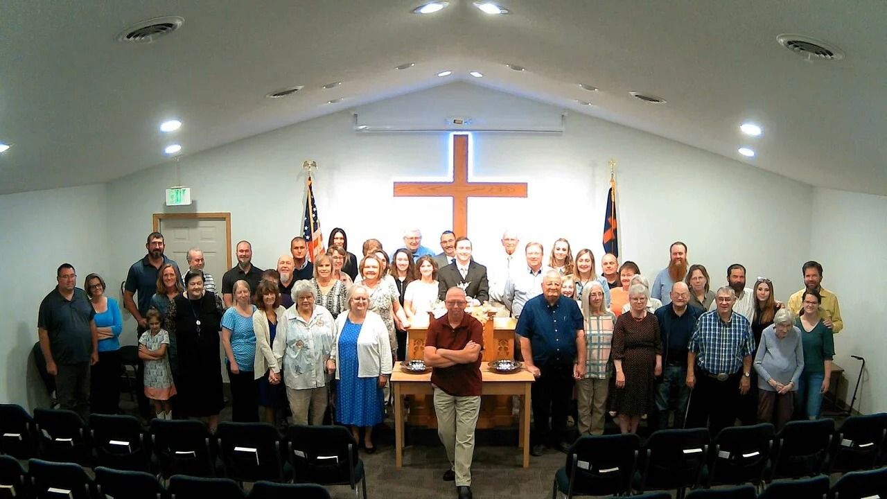 Large group posing in a church sanctuary beneath a glowing cross on the wall.